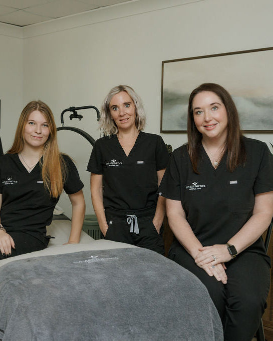 Four women in black uniforms sitting together in a room with medical equipment.
